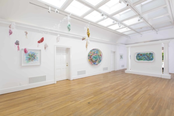 white walled exhibition space with light wooden floors and walls sparsely covered with brightly colored artwork