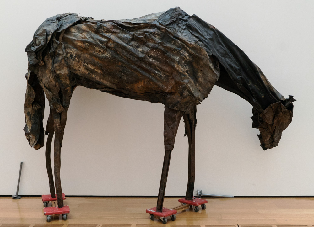 Horse sculpture made of textured sheet metal balancing on dollys during reinstallation