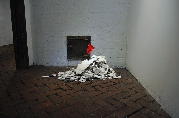 A mound of broken ceramic floor tiles topped with a handmade red flag.