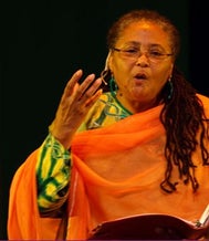 African America middle-aged woman with glasses and an orange wrap, performing.