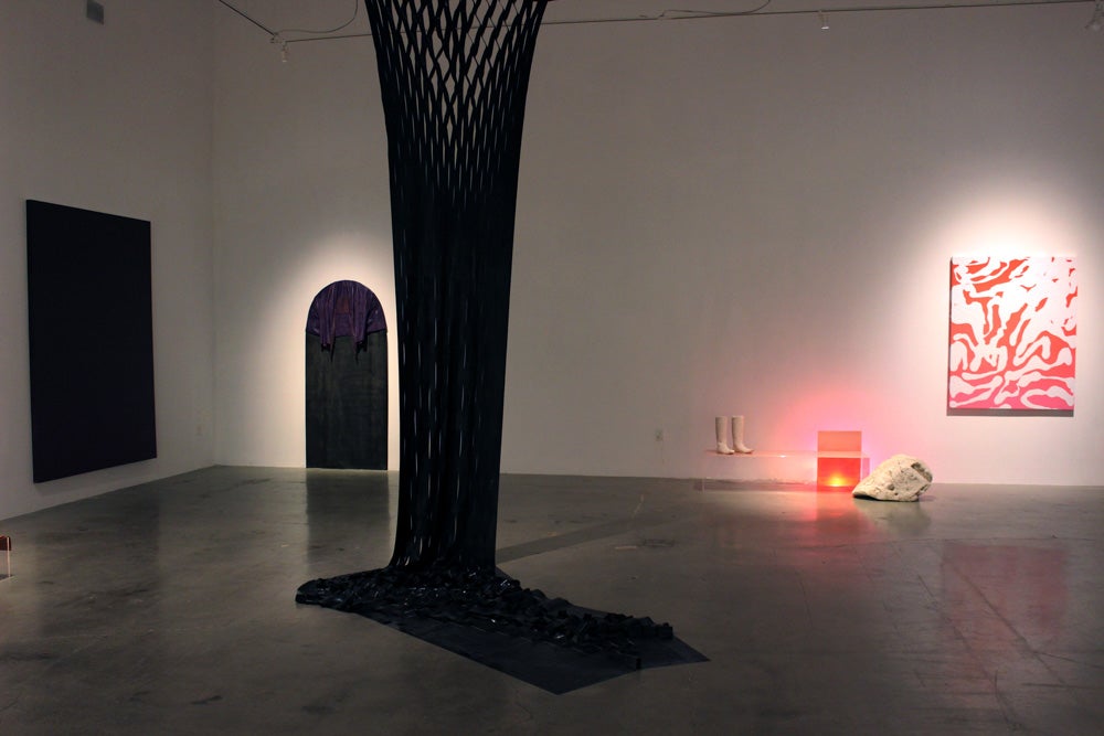 Museum gallery with three wall pieces and a black form suspended in the foreground, by Kirstin MItchell. 