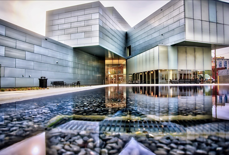 A modern building resembling assymetrically stacked cubes, viewed across and from the level of a pool in front of it. 