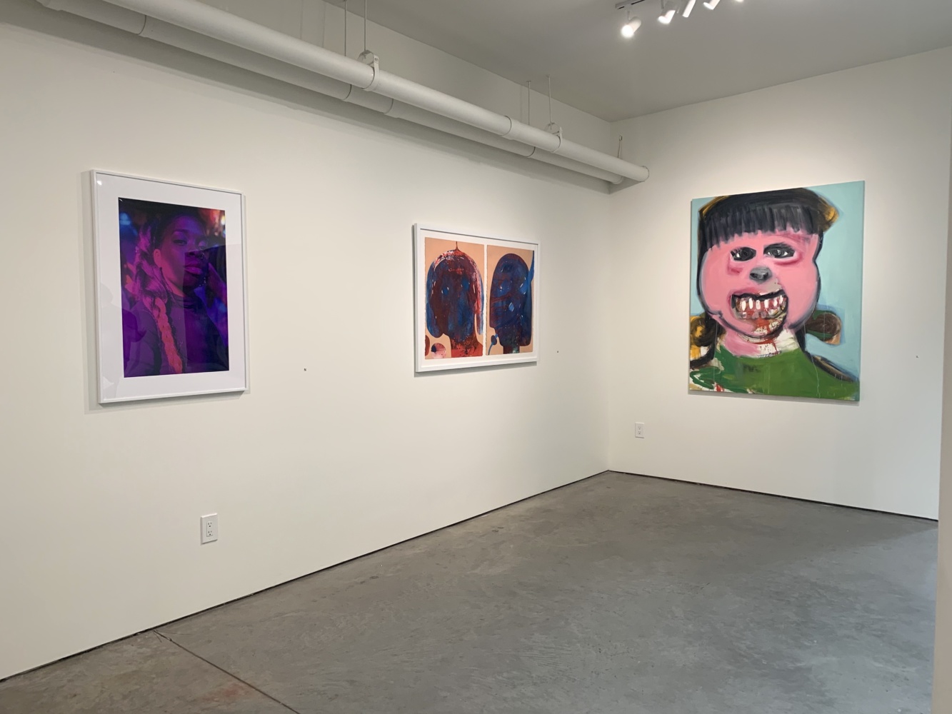 three paints and photographs of people hang in a gallery.
