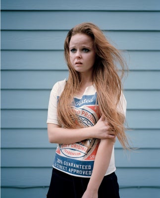 Distraught looking teenage girl with red hair in front of a blue house. 