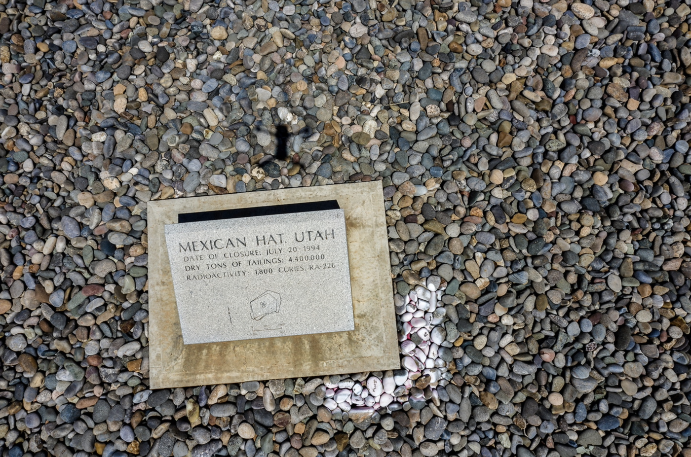 a marker on top of pebbles that reads Mexican Hat, Utah. Date of Closure: July 20 1994. Dry tons of Tailings: 4,400.00. Radioactivity : 1,800 Curies: RA-226