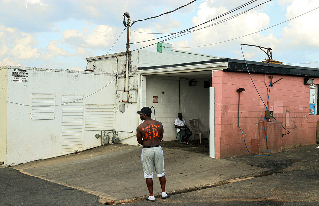 a black man outside of a garage with his back to the camera with orange paint markings.