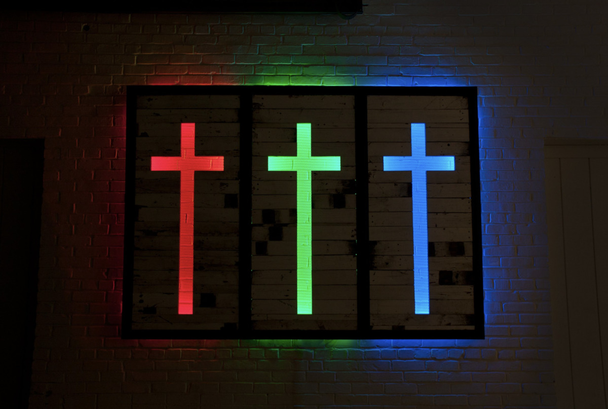 three backlight crucifixes in red, green, and blue light mounted on a wall