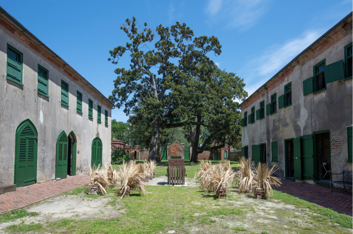 a courtyard with dried fronds and a sculpture, surrounded by brick paths