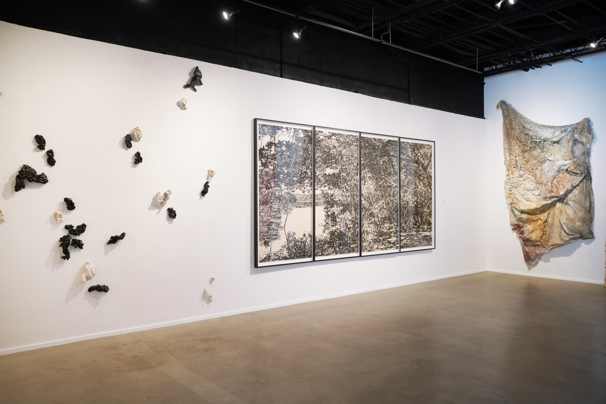 gallery view of three works four paneled woodblock print of mangroves in middle print fabric with mesh and insulation to right and black and white ceramic objects on white wall to left