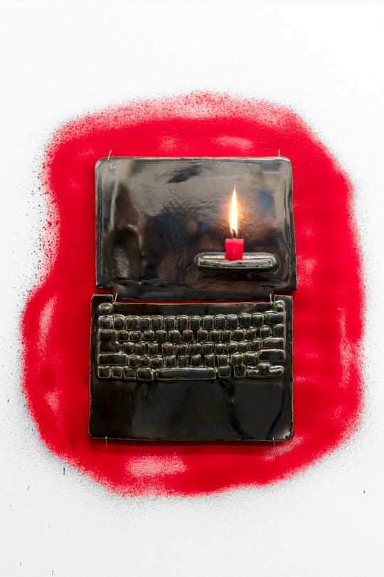 a ceramic model of a laptop on a wall with a short red candle