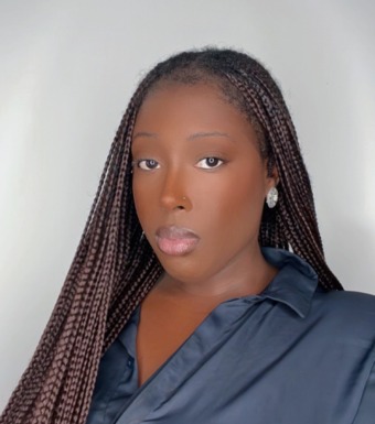Matou wears dark brown box braids and a silky black shirt, she looks inquisitively at the camera