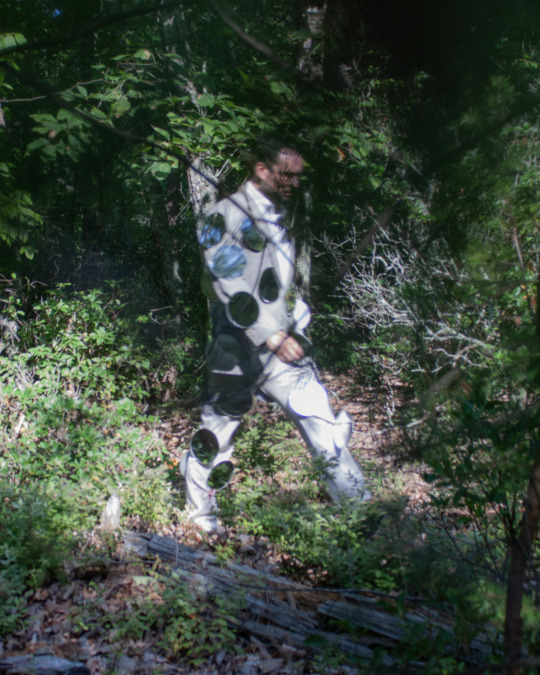 man with mirrors attached to his suit walks around forest